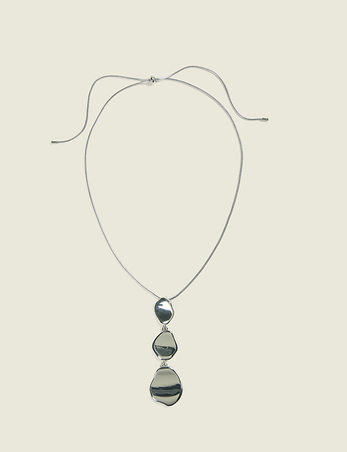 A silver pendant necklace with three irregular, polished stones hangs against a plain, light beige background.