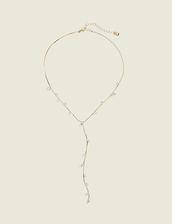 A delicate gold necklace with scattered clear crystals hangs against a plain, light beige background.