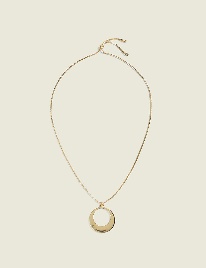 A gold oval pendant hangs from a delicate gold chain against a plain, light beige background.