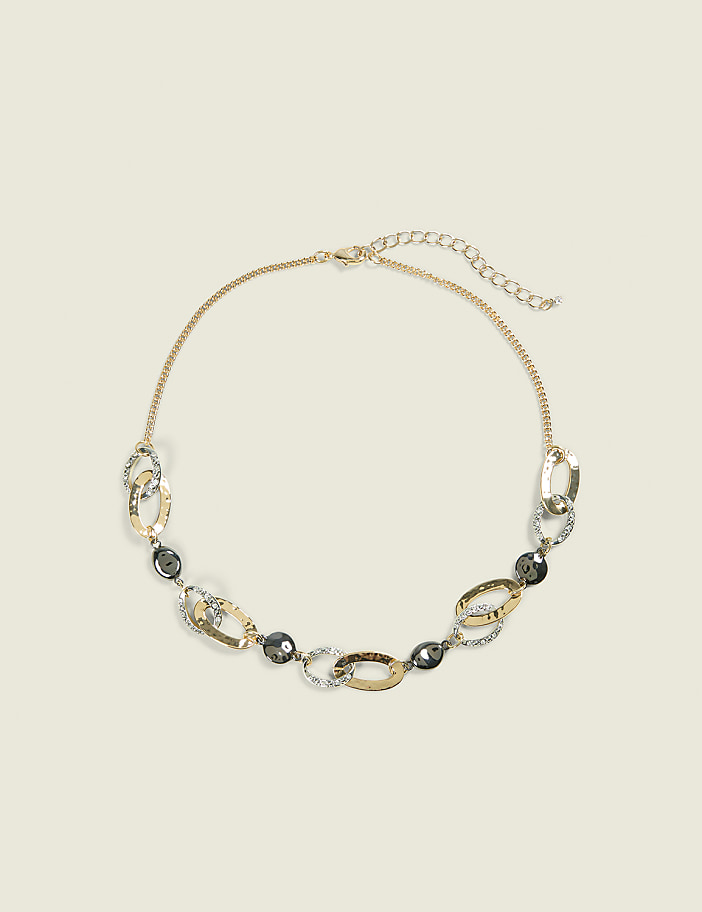 A gold-toned necklace with oval links and dark gray beads rests on a plain, light beige background.