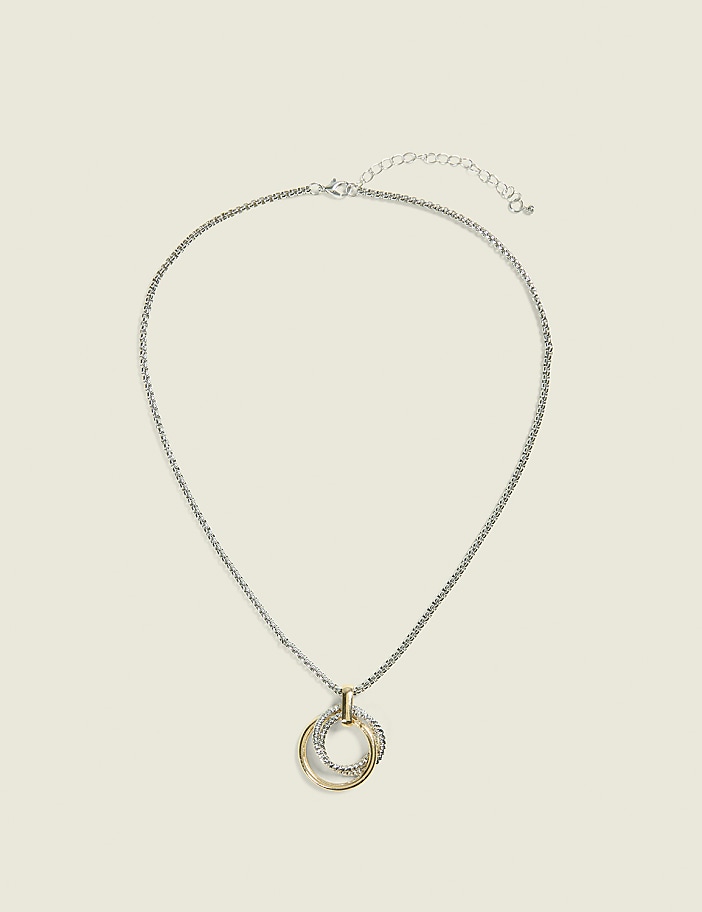A silver chain necklace with a gold and silver interlocking pendant rests against a plain, light beige background.