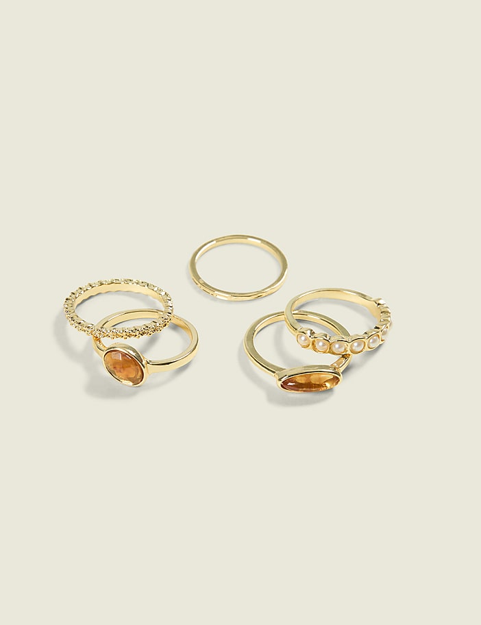 Several gold rings, some adorned with stones and pearls, are arranged on a plain, light-colored background.
