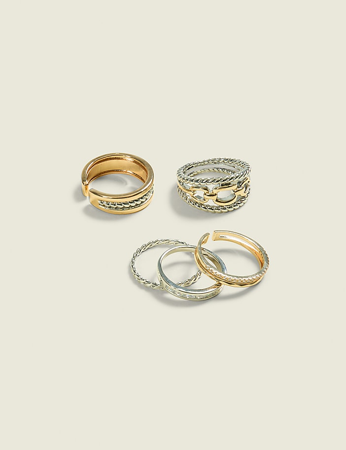 Four rings, two gold and two silver, are arranged on a pale, textured background.