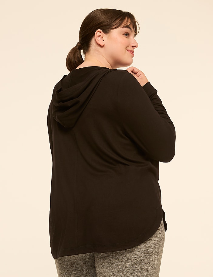 A woman in a black hoodie and grey leggings stands against a plain, light-colored background.