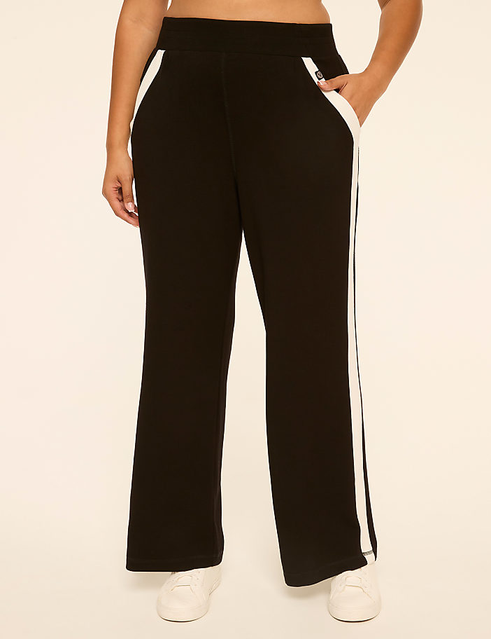 A person wearing black athletic pants with white stripes stands against a plain, light-colored background.