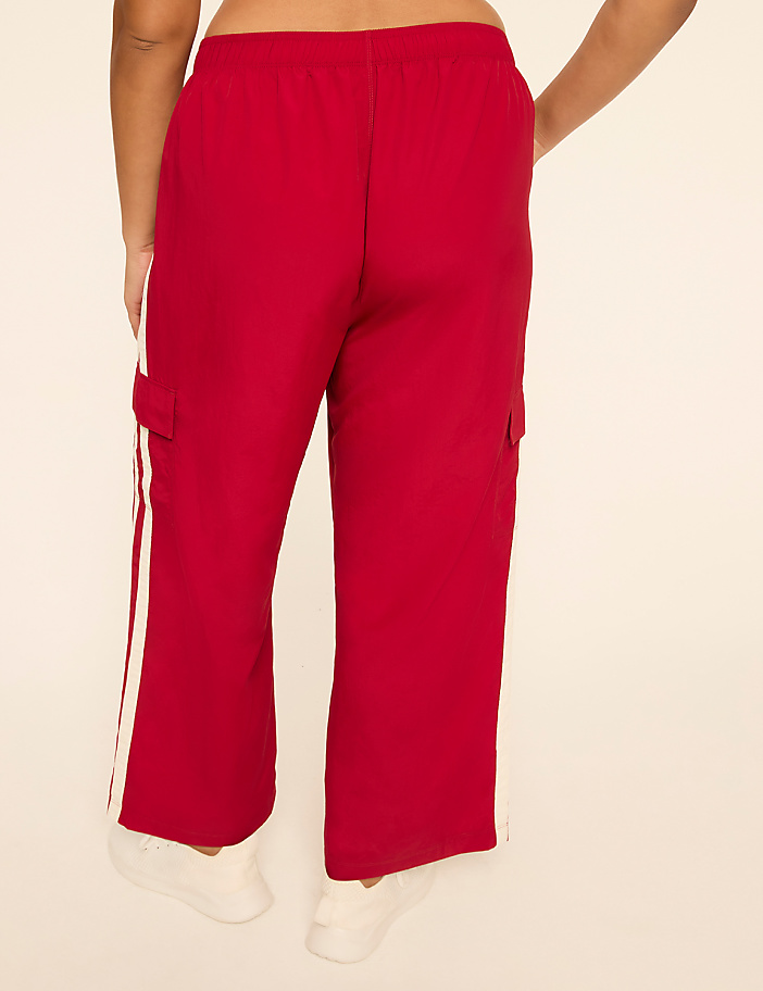 A person wearing red cargo pants with white stripes stands against a plain, light-colored background.