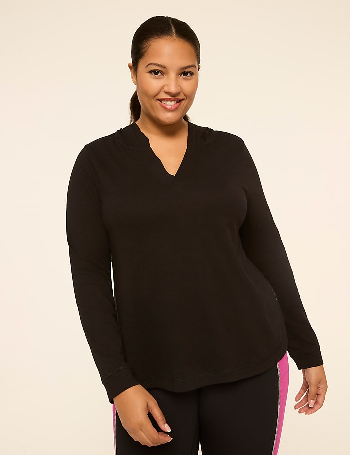 A smiling woman in a black hoodie and athletic leggings stands against a plain, light-colored background.