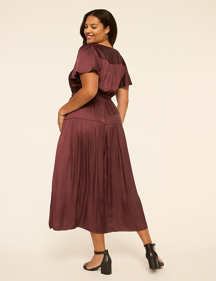 A woman in a burgundy dress poses against a plain, light-colored background.