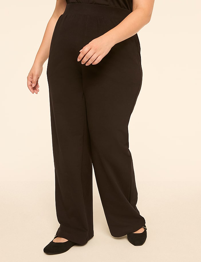 A person in black pants and ballet flats stands against a plain, light-colored background.