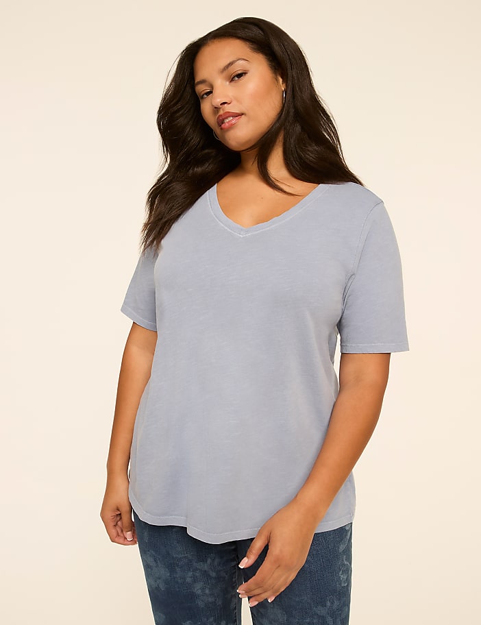 A woman in a light blue v-neck t-shirt and patterned jeans stands against a plain, light-colored background.
