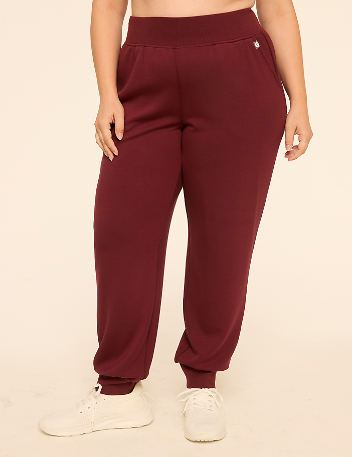 A person wearing maroon sweatpants and white sneakers stands against a plain, light-colored background.