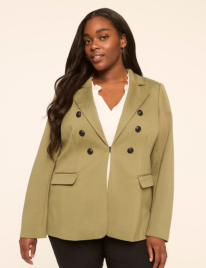 A woman in a green blazer stands against a plain, light-colored background.