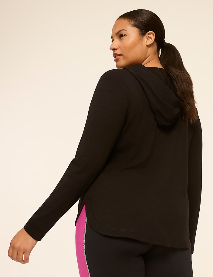 A woman in a black hoodie and leggings stands against a plain, light-colored background.
