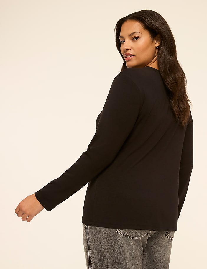 A woman in a black long-sleeved shirt and grey jeans is shown from the side against a plain, light-colored background.
