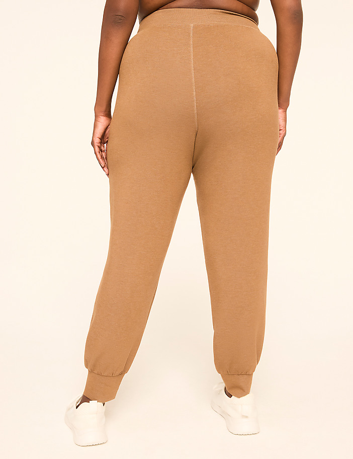 A person wearing tan sweatpants and white sneakers stands against a plain, light-colored background.