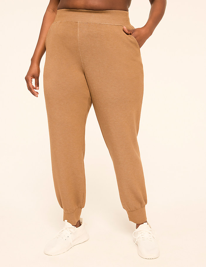 A person wearing tan sweatpants and white sneakers stands against a plain, light-colored background.