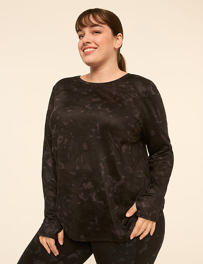 A smiling woman in a black patterned long-sleeved shirt and leggings stands against a plain, light-colored background.