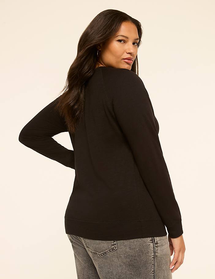A woman in a black sweater and grey jeans poses against a plain, light-colored background.