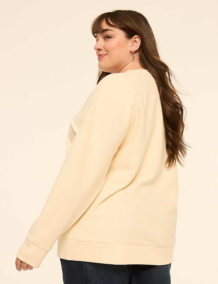 A woman in a cream-colored sweatshirt and dark jeans is shown from the side against a plain, light-colored background.