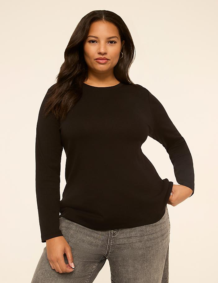 A woman with dark hair and a black long-sleeved shirt stands against a plain, light-colored background.