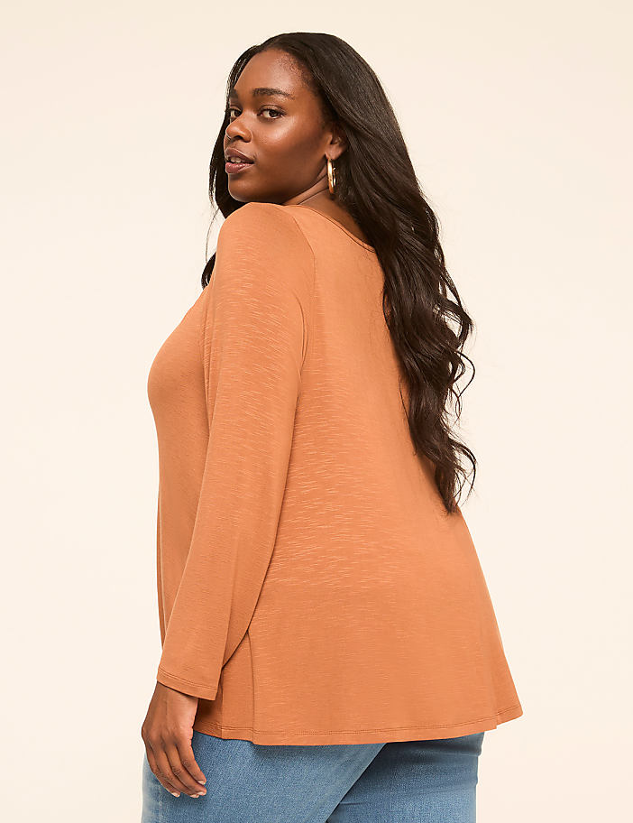 A woman in a rust-colored top and blue jeans poses against a plain, light-colored background.