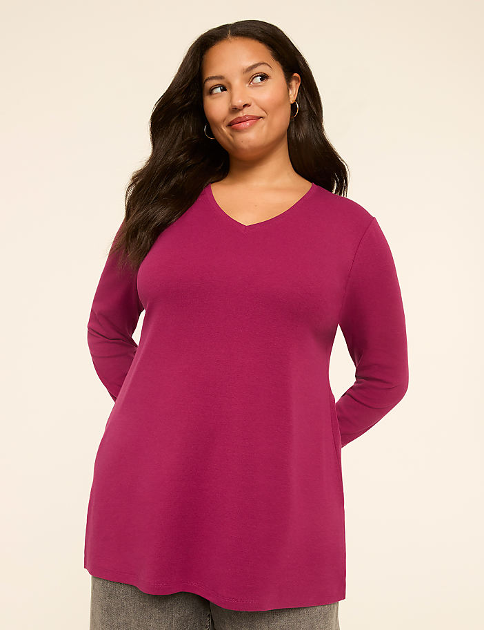 A woman in a magenta v-neck shirt stands against a plain, light-colored background.