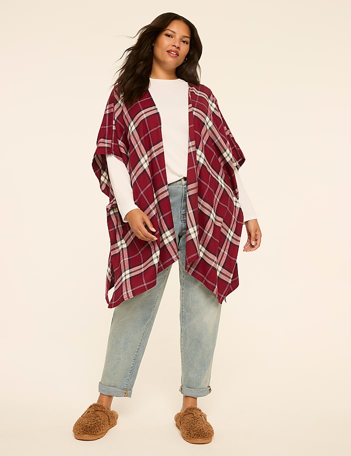 A woman in a plaid poncho and jeans stands against a plain, light-colored background.
