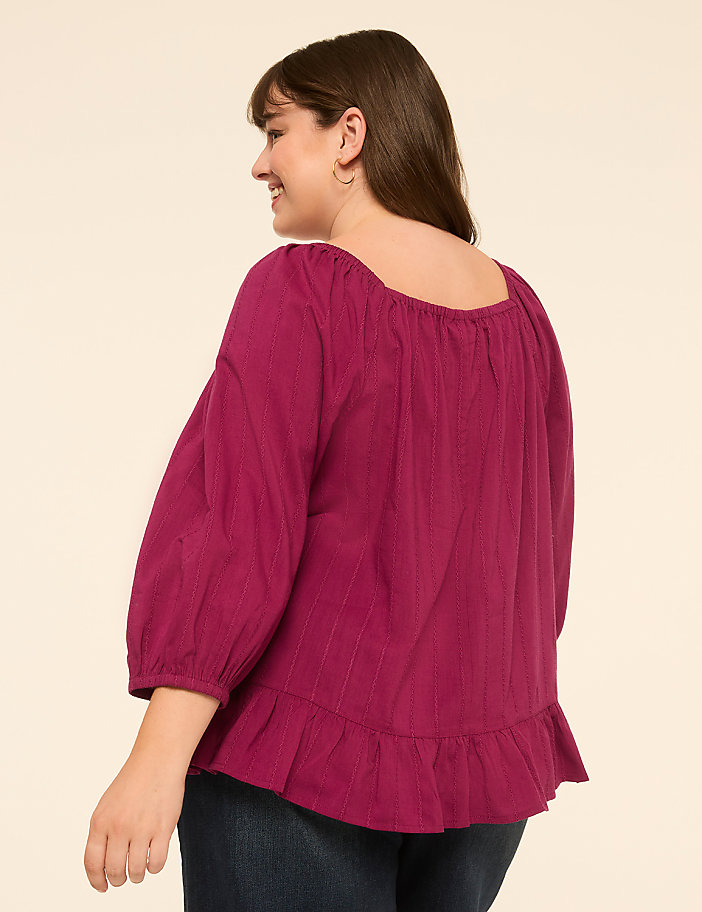A woman in a magenta peasant blouse stands against a plain beige background.