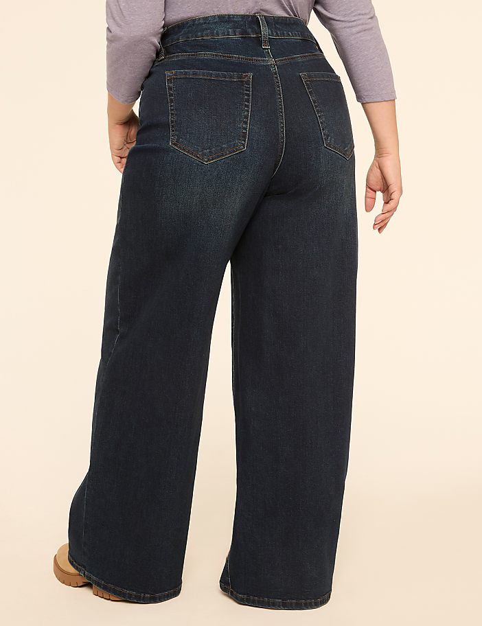 A person wearing dark wash wide-leg jeans stands against a plain, light-colored background.