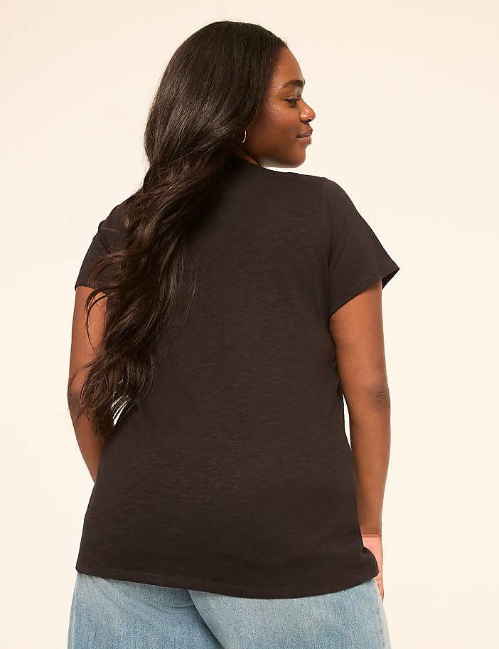 A woman in a black t-shirt and blue jeans stands against a plain, light-colored background.
