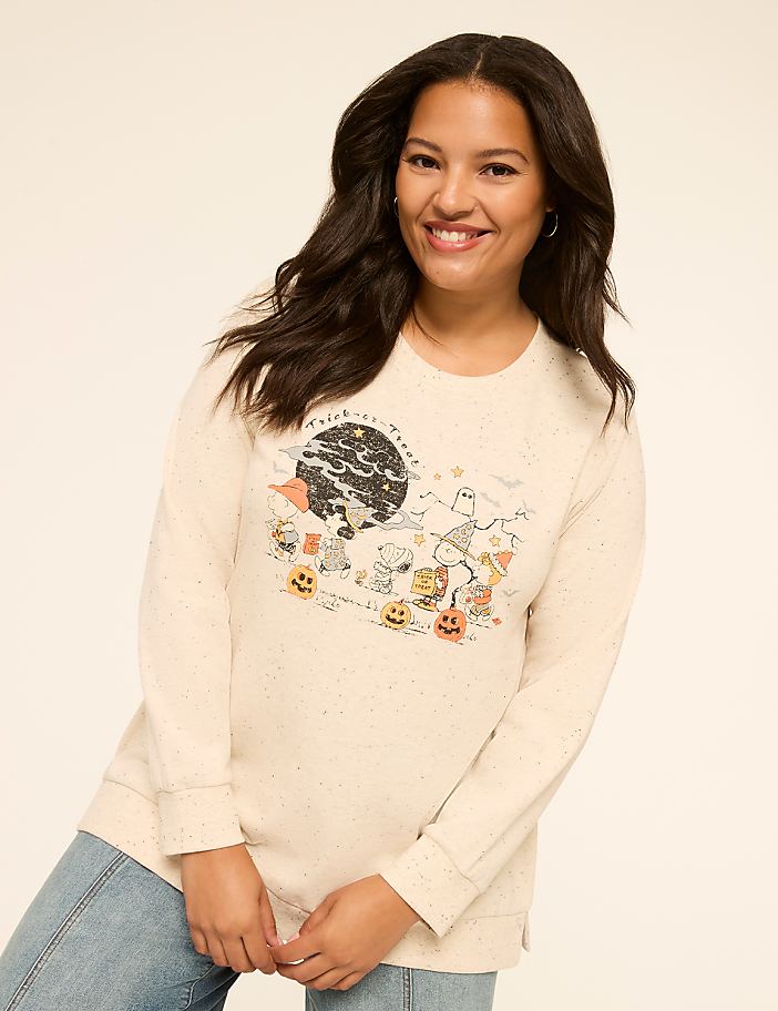 A smiling woman in a cream-colored sweatshirt with a Halloween-themed graphic stands against a plain background.