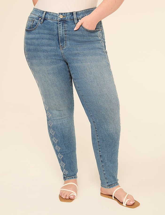 A person in light blue jeans with a diamond pattern on the left leg stands against a plain, light beige background.