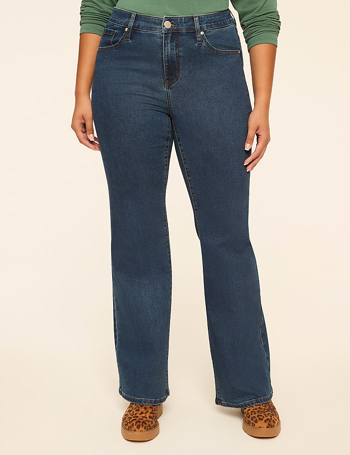 A person wearing dark wash bootcut jeans and leopard print shoes stands against a plain, light-colored background.