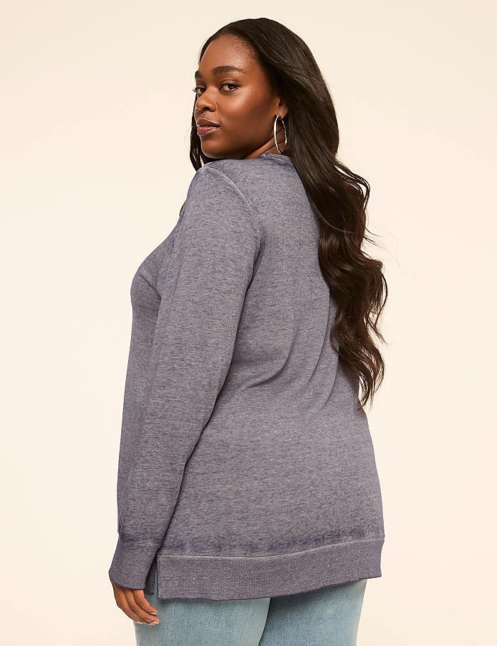 A woman in a blue sweatshirt and jeans stands against a plain, light-colored background.