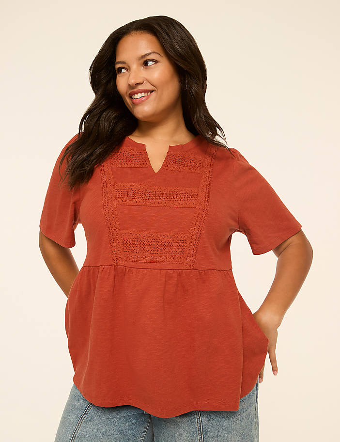 A smiling woman in a rust-colored peasant top stands against a plain, light-colored background.