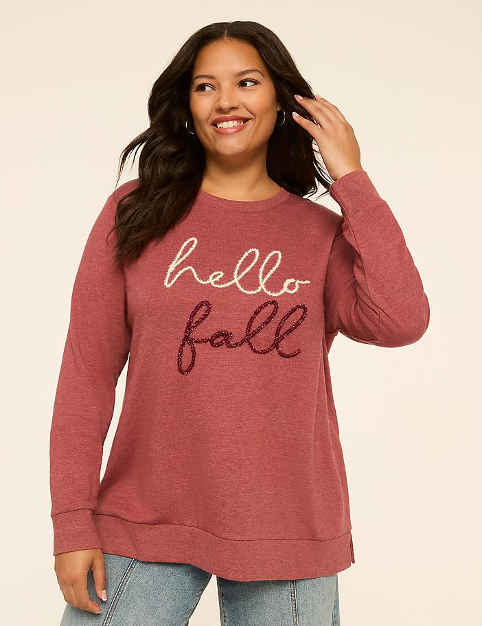A smiling woman in a maroon "hello fall" sweatshirt stands against a plain, light-colored background.