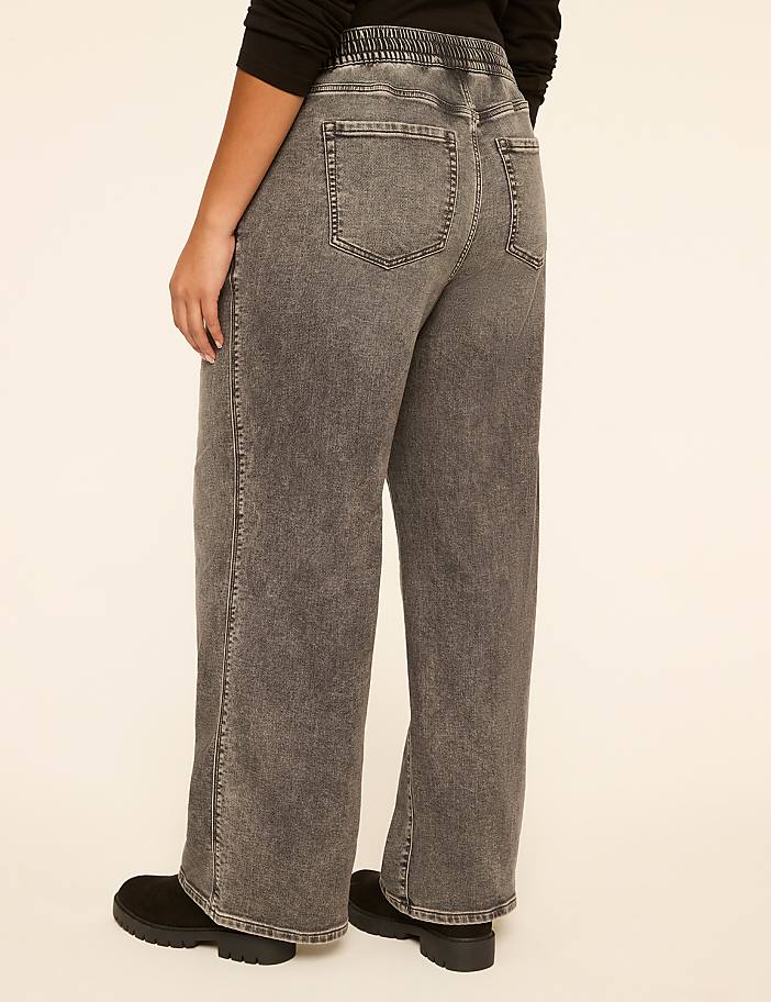 A person wearing acid-wash denim pants and black boots stands against a plain, light-colored background.