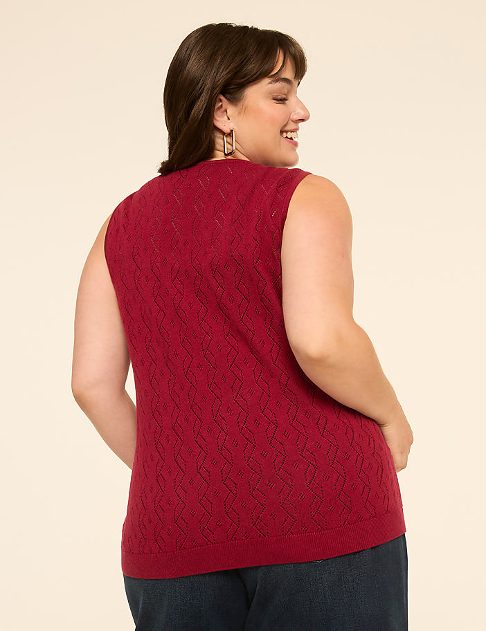 A woman in a red knit vest stands against a plain beige background.