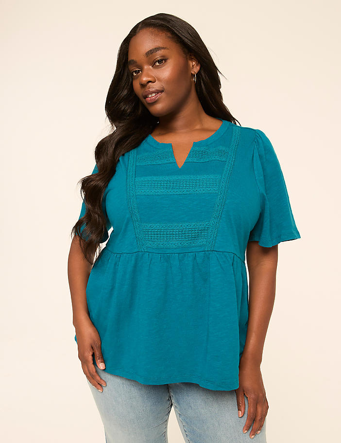 A woman in a teal top and jeans stands against a plain, light-colored background.