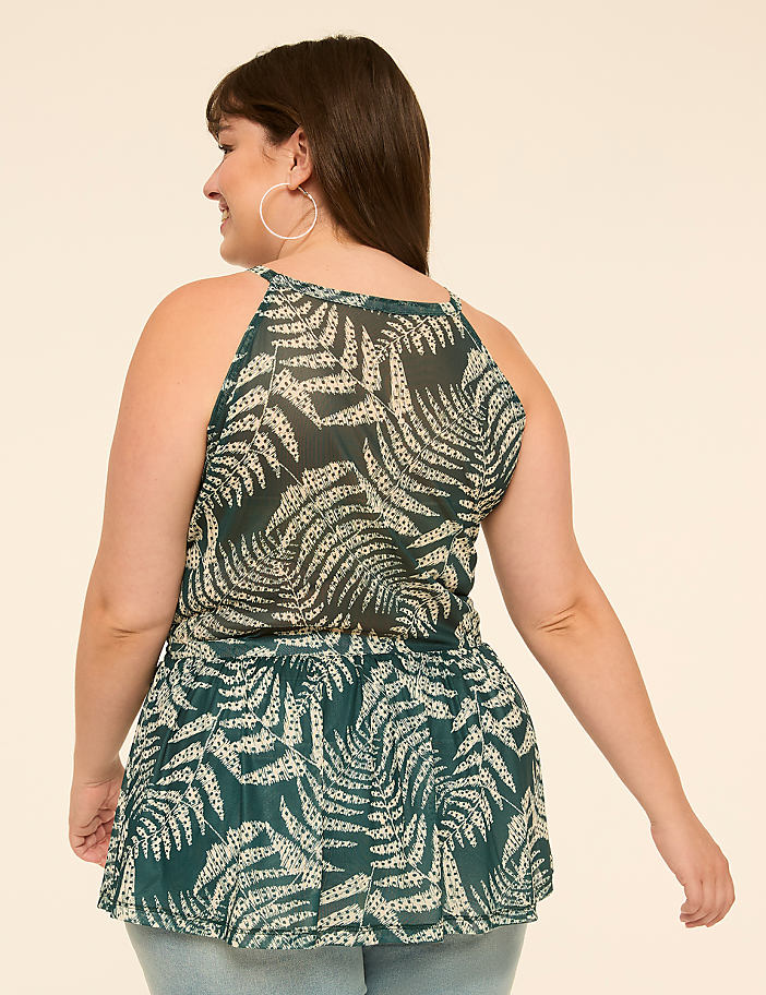 A woman in a green fern-patterned top stands against a plain, light-colored background.