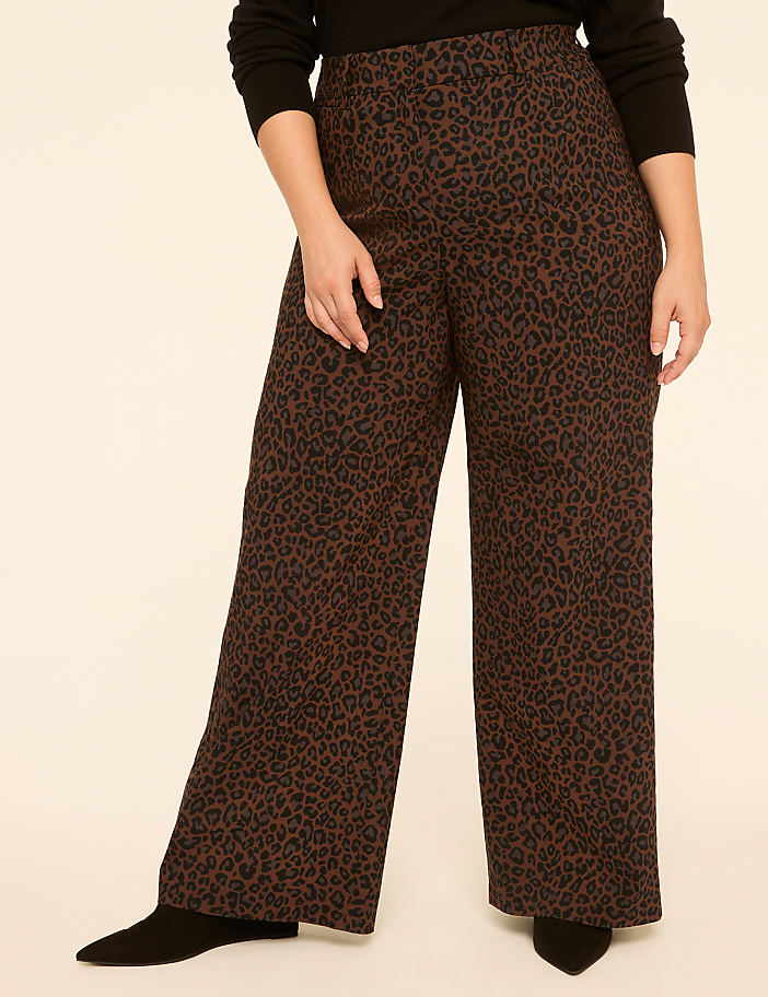 A person stands in the foreground wearing wide-leg leopard print pants and black boots, against a plain, light-colored background.