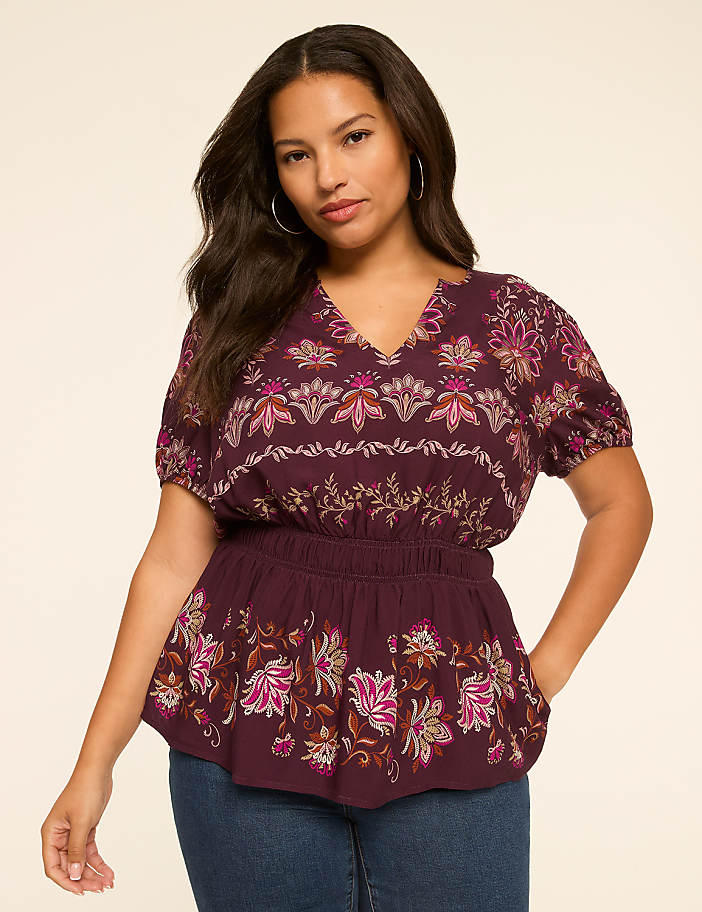 A woman in a floral print peplum top stands against a plain, light-colored background.
