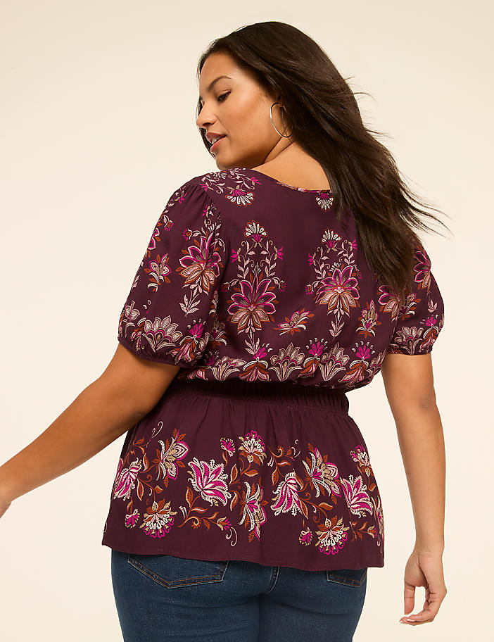 A woman in a floral print top and jeans is shown from the back against a plain, light-colored background.