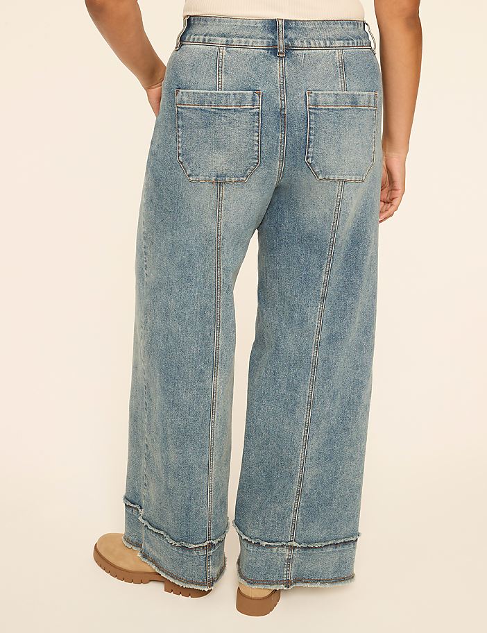 A person wearing wide-leg, light-wash denim jeans with frayed hems stands against a plain, light-colored background.