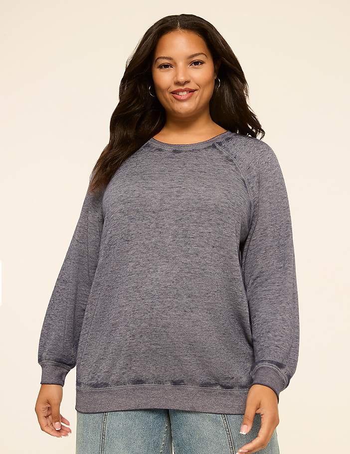 A smiling woman in a gray sweatshirt stands against a plain, light-colored background.