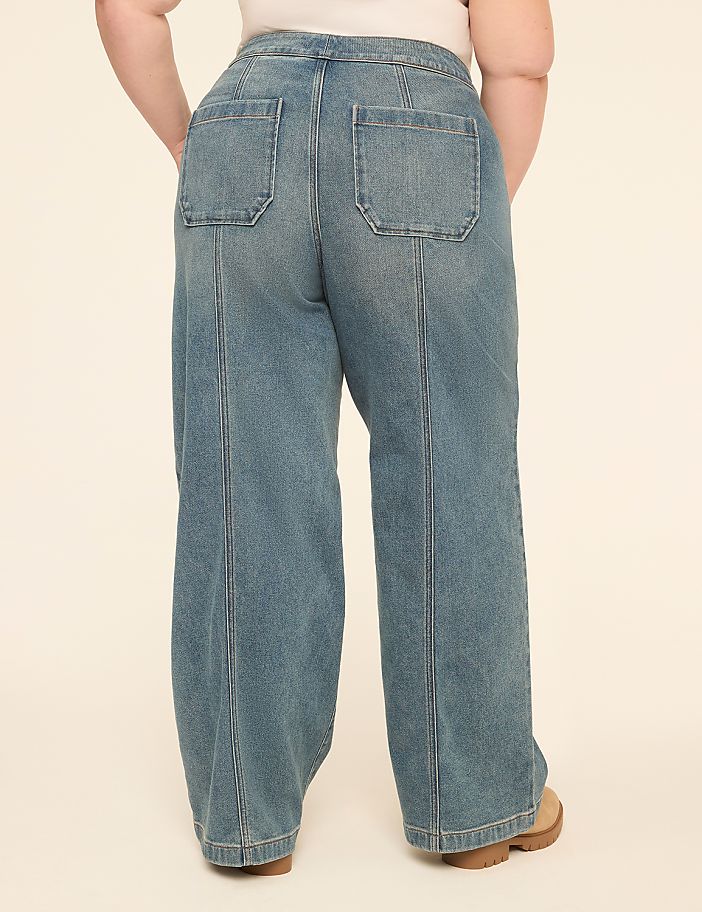 A person stands in light-wash denim wide-leg jeans with a plain background.