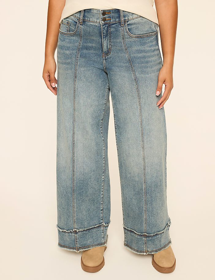 A person stands in light-wash wide-leg jeans with frayed hems and tan shoes against a plain cream background.