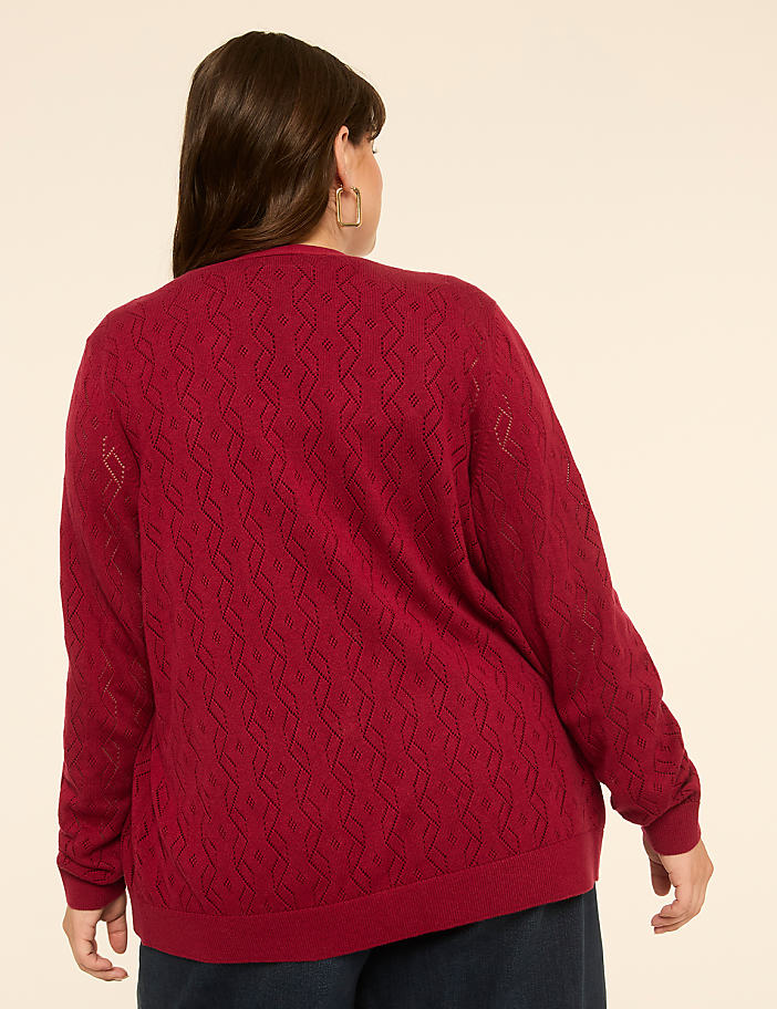 A woman in a red, patterned sweater stands against a plain, light-colored background.