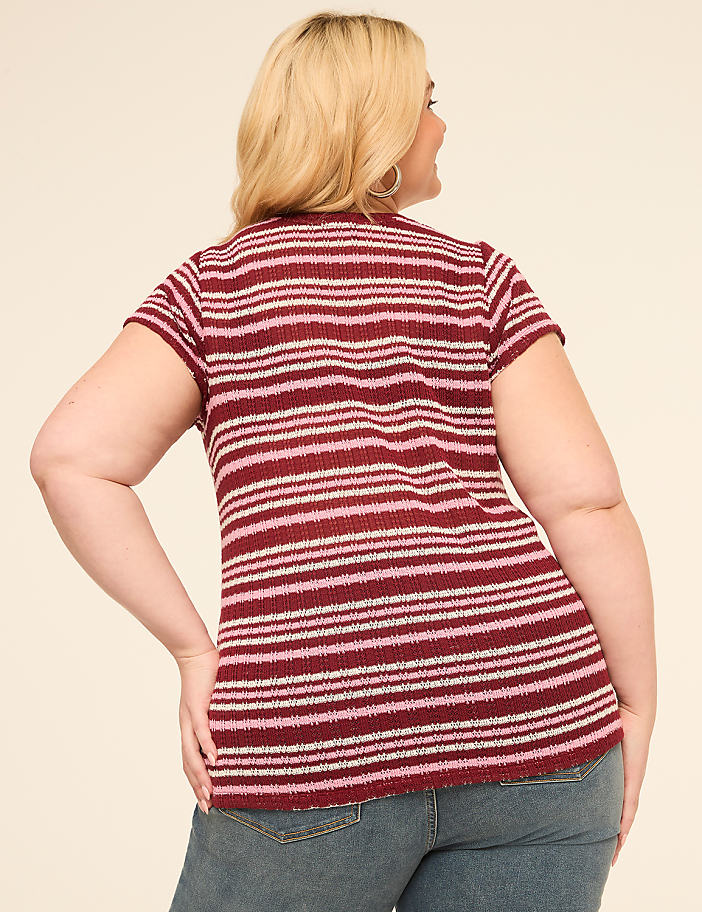 A woman in a striped shirt and jeans stands against a plain, light-colored background.