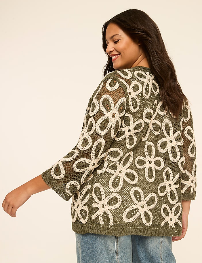 A woman in a floral cardigan stands against a plain, light-colored background.